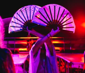 A person holding up two large fans while illuminated by bright lights