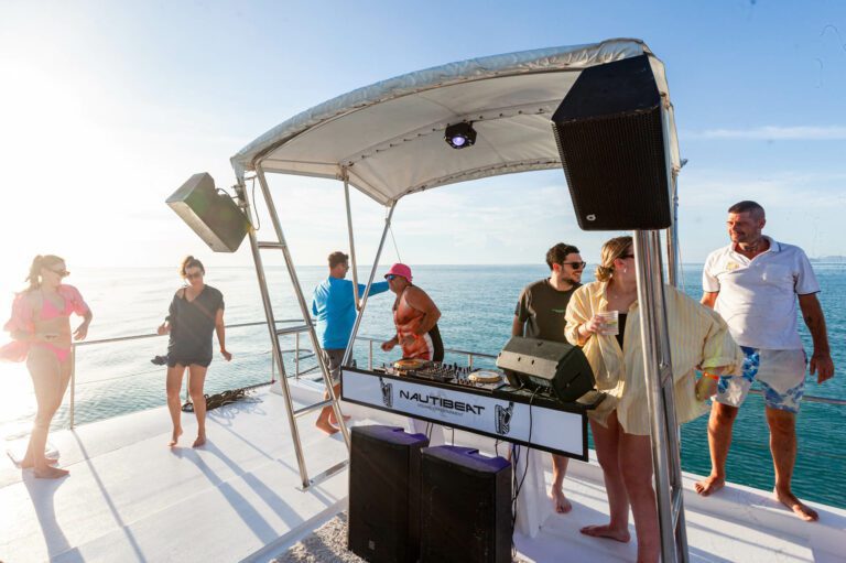 A group of people dancing around the DJ area of a boat
