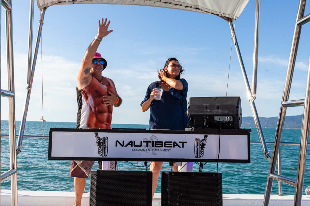 Two people standing behind a DJ area aboard a party boat